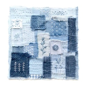 Può includere: Un pezzo tessile quadrato composto da vari ritagli di tessuto in tonalità blu cuciti insieme. Il patchwork presenta diversi motivi di ricamo bianco, tra cui croci, linee, motivi floreali e forme geometriche con bordi sfilacciati.