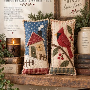 May include: Two rectangular fabric pillows with frayed edges. One features a blue background with a house, chimney, and fence. The other has a cream background with red stripes, a red cardinal bird on a branch with green leaves and red berries.