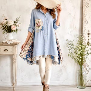 May include: A light blue button-down shirt with a vertical pinstripe pattern, featuring a floral patch pocket on the chest and multi-patterned floral fabric panels on the sides. The shirt has a high-low hemline with frayed edges and long sleeves.