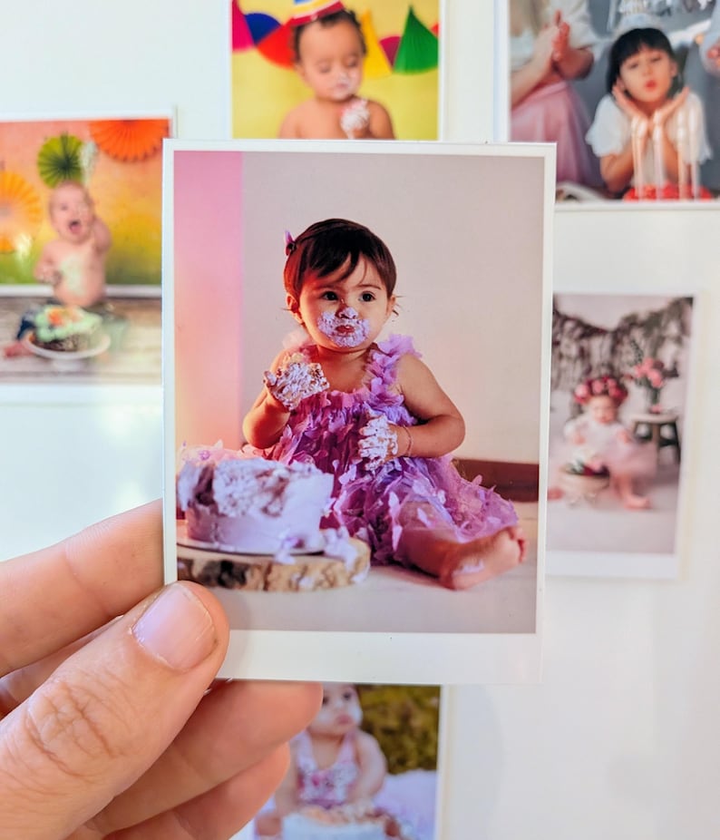 May include: A photograph of a baby girl covered in purple frosting, sitting in front of a cake. The girl is wearing a purple dress and has frosting on her face and hands. Other photos are visible in the background.