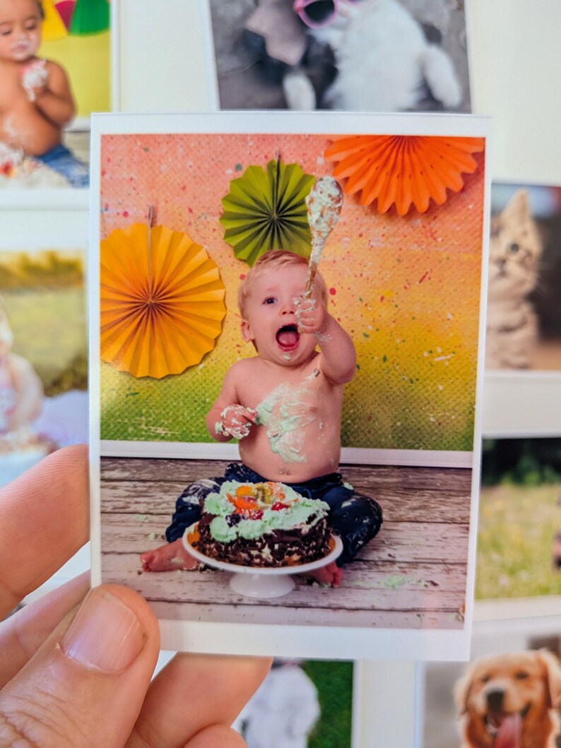 May include: A photograph of a baby celebrating a birthday. The baby is covered in frosting and holding a spoon. A chocolate cake with green frosting and fruit sits on a white cake stand. Colorful paper fans decorate the background.