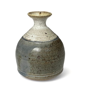 Puede incluir: Un jarrón pequeño, redondo, de cerámica con un esmalte marrón claro, blanco y azul. El jarrón tiene un cuello estrecho y una base ancha.