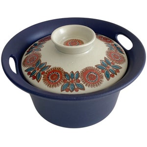 以下が含まれることがあります： 赤、オレンジ、青、緑の色合いの花柄が描かれた白い蓋が付いた青いセラミック製のキャセロール