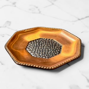 May include: An octagonal tray featuring a smooth, metallic copper-toned border with a beaded edge. The centre of the tray is a recessed, hexagonal panel with a dark, textured, hammered finish that contrasts with the polished outer rim.
