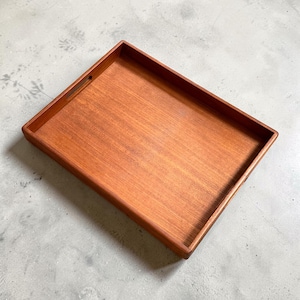 May include: A rectangular wooden tray with a rich, reddish-brown finish. The tray has a raised edge and a small handle cut out on one side. The wood grain is visible, adding to the tray's natural aesthetic. Ideal for serving or display.