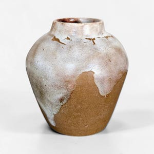 May include: A ceramic vase with a wide, rounded body and a short, narrow neck. The lower portion features a raw, earthy brown clay texture, while the upper section is coated in a thick, drippy white glaze that reveals subtle brown crackle patterns.