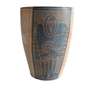 Pode incluir: Um vaso de cerâmica com um design geométrico azul e castanho. O vaso apresenta uma figura humana estilizada com um padrão circular no peito.