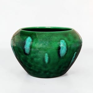 May include: A round, green ceramic bowl with a glossy finish. The bowl has a dark green base color with lighter green and turquoise accents. The interior is a dark, glossy black.