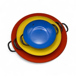 May include: A nested set of three colorful pans. The largest is red, the middle is yellow, and the smallest is blue. Each pan has a black handle on either side. The pans are arranged in a stack, with the largest on the bottom.