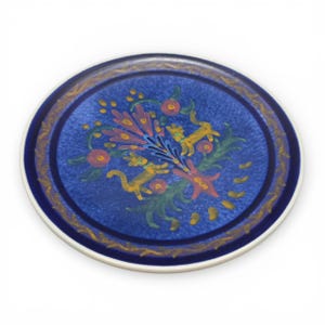 May include: Round ceramic plate with a blue center and a white rim. The blue center features a floral design with yellow, pink, and green accents. A gold border surrounds the central design.