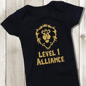 Op de afbeelding: Zwarte baby romper met een gouden leeuwenembleem en de tekst "Level 1 Alliance".