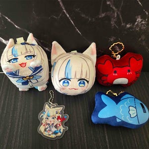 May include: A selection of plush keyrings and an acrylic charm featuring anime-style characters. The plush toys include a white cat-eared character with blue accents, a red crab, and a blue fish. The acrylic charm depicts a similar character.