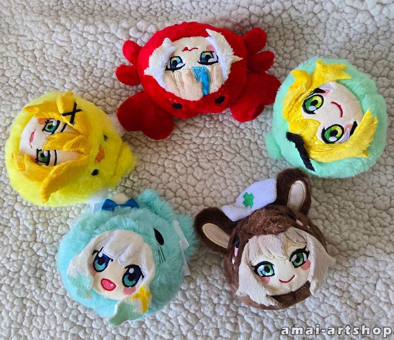 May include: Five round plush toys featuring anime-style faces. One is a red crab, one is a yellow chick, one is a light green creature, one is a light blue creature with white hair, and one is a brown animal with a white hat. Text reads amai-artshop.