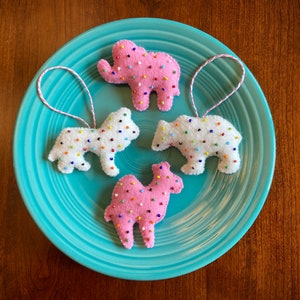 May include: Four felt ornaments shaped like an elephant, a bear, a camel, and a dog. Each ornament is covered in white felt and decorated with colorful sprinkles.