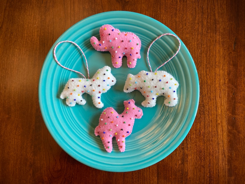 May include: Four felt ornaments shaped like an elephant, a bear, a camel, and a dog. Each ornament is covered in white felt and decorated with colorful sprinkles.