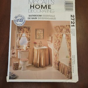 May include: A McCall's Home Decorating pattern envelope featuring a bathroom scene. The image shows a bathroom set with floral curtains, a sink skirt, and matching toilet seat cover. The text reads "Bathroom Essentials".