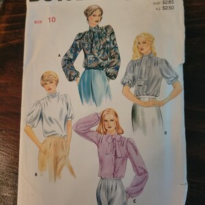 Può includere: Un modello di cucito Butterick vintage, taglia 10, con illustrazioni di camicette di vari stili. Il modello include una camicetta a collo alto con stampa paisley, una camicetta azzurra con maniche a sbuffo e una camicetta rosa con fiocco.