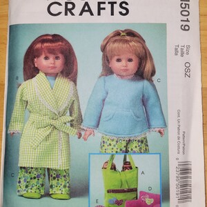 May include: A sewing pattern for making doll clothes. The pattern includes instructions for making a green and white checkered robe, a blue and white patterned pajama top, and a green and white patterned pajama bottom. The pattern also includes instructions for making a green tote bag, a pink pillow, and a pink sleeping bag.