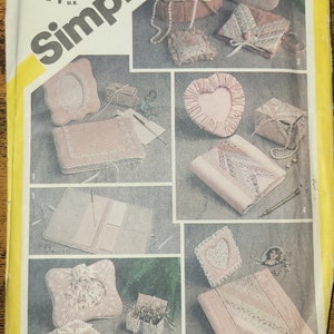 May include: A Simplicity sewing pattern for making five different types of decorative boxes. The pattern includes a heart-shaped box, a rectangular box, a square box, and two different types of photo albums. The pattern is printed on a yellow background with a white border. The pattern number is 5296. The price is $3.50 USD and £1.25 GBP. The pattern is designed by Marjorie Puckett.