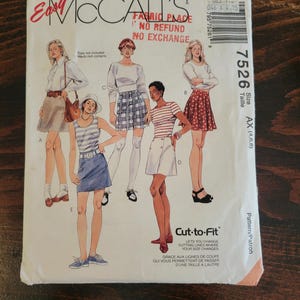 Puede incluir: Un sobre de patrón de costura McCall's vintage con ilustraciones de varias combinaciones de faldas y tops. El número de patrón es 7526, con el rango de tallas AX (4,6,8). El sobre incluye el texto "Fabric Place" y "No Refund No Exchange".