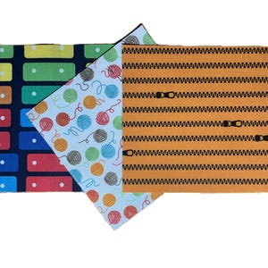 Puede incluir: Tres muestras de tela rectangulares con patrones distintos: un fondo azul oscuro con rect&aacute;ngulos coloridos, un fondo azul claro con ovillos de lana multicolores y un fondo naranja con motivos de cremalleras negras horizontales.