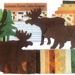 May include: A table runner kit with the text "Autumn Forest Table Runner". The kit includes brown moose and bear shapes, green tree shapes, and various fabric squares in fall colors. The kit is designed for an 8-inch table runner.