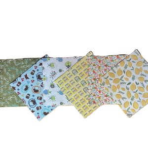 Puede incluir: Un juego de cinco servilletas de tela cuadradas con patrones distintos: verde oliva con gafas blancas, azul claro con h&aacute;msteres marrones, blanco con escarabajos coloridos, amarillo con frascos y blanco con limones amarillos y hojas verdes.