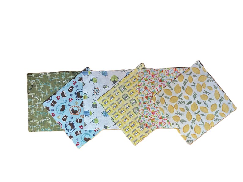 Puede incluir: Un juego de cinco servilletas de tela cuadradas con patrones distintos: verde oliva con gafas blancas, azul claro con h&aacute;msteres marrones, blanco con escarabajos coloridos, amarillo con frascos y blanco con limones amarillos y hojas verdes.