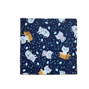 Puede incluir: Una pieza de tela cuadrada con fondo azul oscuro y un patr&oacute;n repetitivo de gatos de dibujos animados de color gris claro en varias posturas, algunos sentados dentro de cajas de cart&oacute;n marrones, intercalados con peque&ntilde;as estrellas, corazones y nubes blancas.