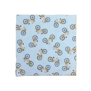 Puede incluir: Una pieza cuadrada de tela azul claro con un patr&oacute;n repetitivo de bicicletas de color amarillo mostaza. Cada bicicleta est&aacute; ilustrada con l&iacute;neas finas, incluyendo ruedas, un marco y una peque&ntilde;a cesta, orientadas en varias direcciones.