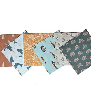 Puede incluir: Una colecci&oacute;n de seis estuches de tela rectangulares con varios patrones, incluyendo suricatos sobre fondo terracota, narvales azules, rodajas de naranja, piratas sobre azul claro, p&aacute;jaros sobre crema y arco&iacute;ris sobre fondo verde oscuro.