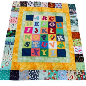 May include: A colorful alphabet quilt with a yellow border and a patchwork design. The letters are in a grid pattern on a green background.