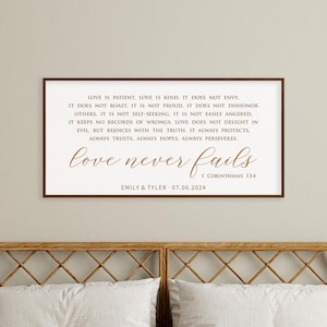 May include: A framed print featuring the text "Love is Patient, Love is Kind" and "love never fails" in a brown script font. The names "Emily & Tyler" and the date "07.06.2024" are below the text. The frame is brown.