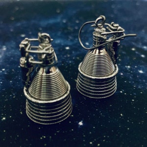 Puede incluir: Un par de pendientes de motor de cohete de plata. Los pendientes son detallados y tienen un aspecto realista.