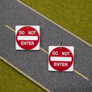 May include: Two red and white "Do Not Enter" signs with a white bar across the middle. The signs are on a gray asphalt surface with a yellow line.