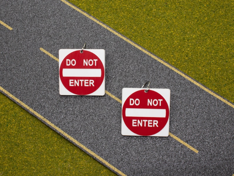 May include: Two red and white "Do Not Enter" signs with a white bar across the middle. The signs are on a gray asphalt surface with a yellow line.