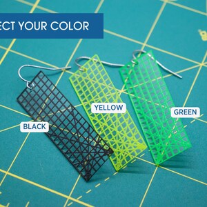 K&ouml;nnte beinhalten: Ohrringe in Schwarz, Gelb und Gr&uuml;n, jeweils mit einem Gittermuster, h&auml;ngen an silbernen Haken. Der Text "SELECT YOUR COLOR" steht oben. Die Ohrringe werden auf einer gr&uuml;nen Schneidematte pr&auml;sentiert.