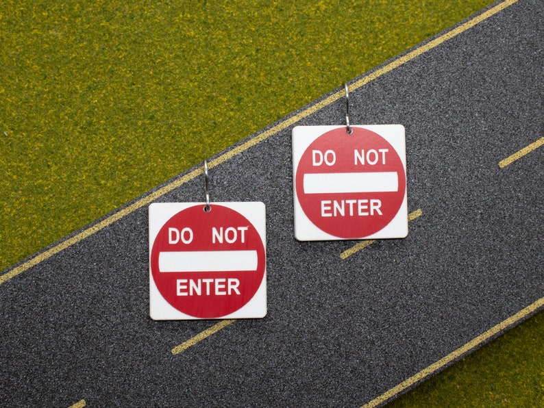 May include: A pair of earrings featuring red and white 'Do Not Enter' signs. The signs are square and have a white bar across the middle.