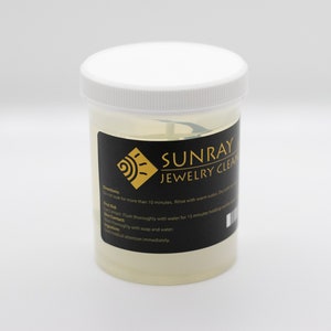 May include: A clear plastic jar with a white lid containing a yellow liquid. The label on the jar is black with gold lettering and reads "SUNRAY JEWELRY CLEAN". The label also includes instructions for using the product.