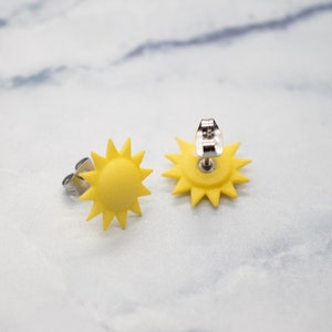 May include: A pair of yellow sun-shaped earrings with silver posts. The earrings are made of polymer clay and have a 3D design.
