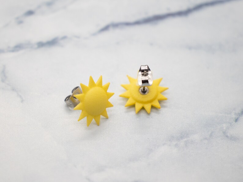 May include: A pair of yellow sun-shaped earrings with silver posts. The earrings are made of polymer clay and have a 3D design.