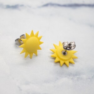 May include: A pair of yellow sun earrings with silver posts. The earrings are shaped like a sun with a starburst design.