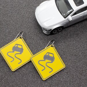 May include: A pair of yellow earrings shaped like a warning sign with a black car icon and the text "Slippery When Wet".