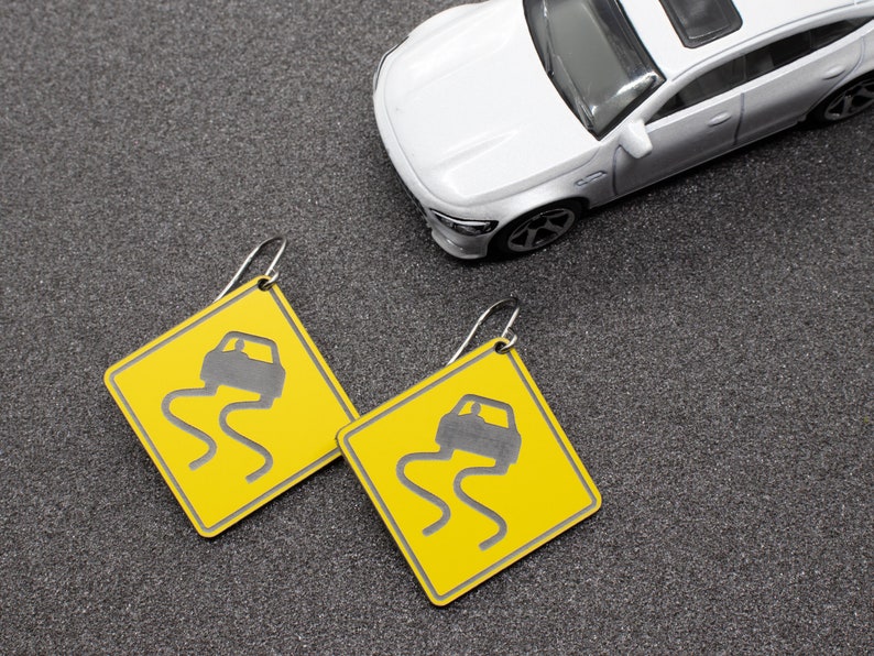 May include: A pair of yellow earrings shaped like a warning sign with a black car icon and the text "Slippery When Wet".
