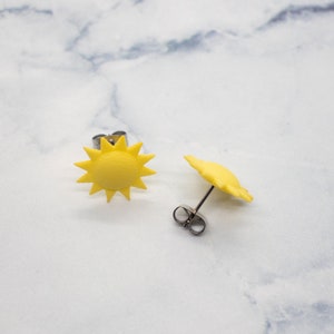 May include: A pair of yellow sun earrings. The earrings are made of polymer clay and have a simple, modern design.