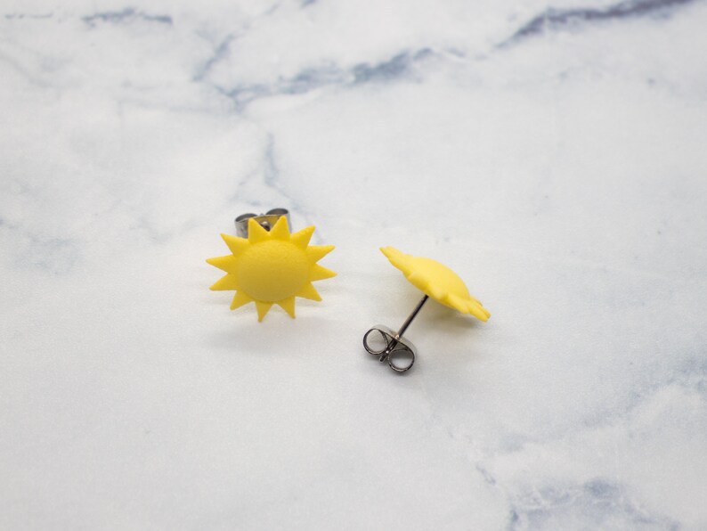 May include: A pair of yellow sun earrings. The earrings are made of polymer clay and have a simple, modern design.
