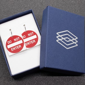May include: A pair of earrings in a blue box. The earrings are shaped like red and white "Do Not Enter" signs.