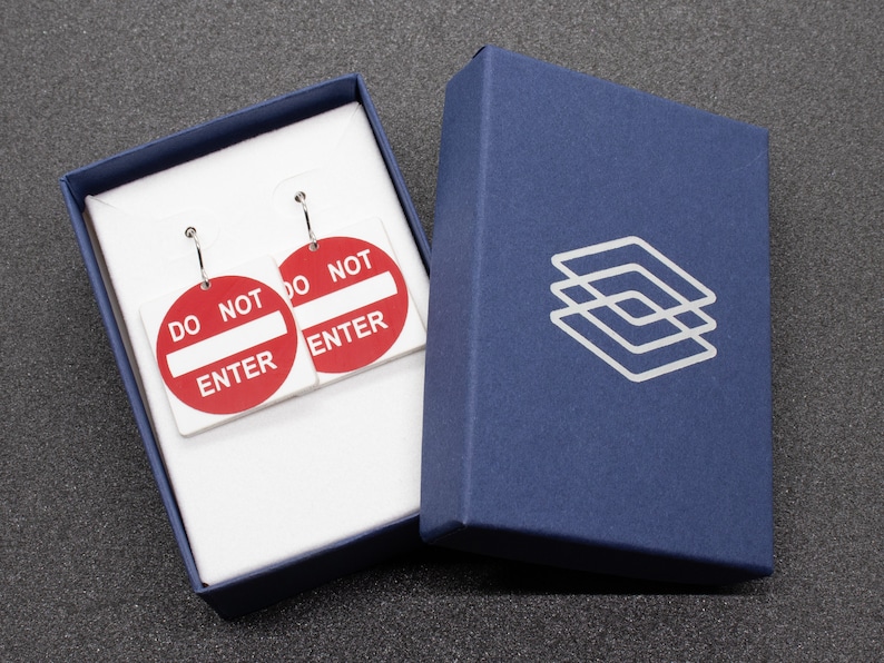 May include: A pair of earrings in a blue box. The earrings are shaped like red and white "Do Not Enter" signs.
