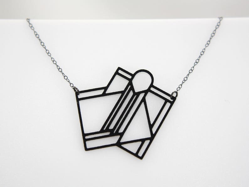 Op de afbeelding: Een zwarte geometrische ketting met een hanger. De hanger is gemaakt van meerdere overlappende vormen die een modern en abstract ontwerp cre&euml;ren.
