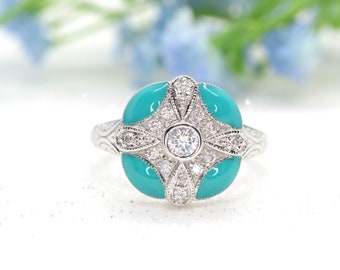 Puede incluir: Un anillo de plata con una piedra turquesa engastada en un diseño floral. El anillo está rodeado de piedras transparentes más pequeñas.